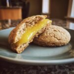Two Lemon Curd Cookies on a plate, one cut in half to show the lemon filling.
