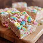Close up of Lucky Charms Rice Crispy Treats showing colorful marshmallows on a wooden board.