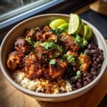 A vibrant bowl of Mexican chicken, black beans, and rice, garnished with cilantro and lime wedges.