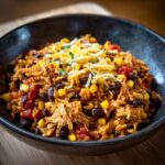 Bowl of Mexican rice and chicken in crockpot, topped with cheese, corn, and black beans.