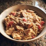 A bowl of One-Pot Chicken Orzo featuring tender chicken, orzo pasta, and diced tomatoes, topped with parmesan cheese.
