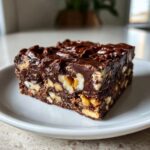 A close-up of a slice of Paula Deen Fudge featuring layers of chocolate, nuts, and a rich, glossy topping.