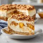 A slice of Peach Cobbler Cheesecake with a graham cracker crust, cheesecake filling, peach cobbler layer, and crumble topping.