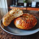 Two halves of a protein bagel on a plate, showing the texture and sesame seed topping.