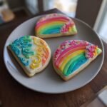 Three rainbow sugar cookies with royal icing for St. Patrick's Day on a gray plate.