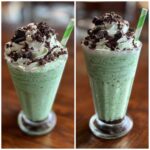 Two glasses filled with a creamy green shamrock shake, topped with whipped cream, chocolate drizzle, and cookie crumbles.