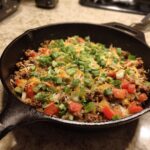 Ground turkey recipe in a skillet with tomatoes, onions, cheese, and green onions.