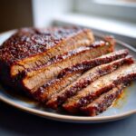 Juicy sliced slow cooker brisket on a gray plate, glistening with sauce.