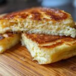 A stack of golden-brown sourdough discard pancakes on a wooden board, drizzled with syrup.