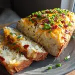 Slices of stuffed potato loaf topped with cheese, bacon, and chives on a gray plate. A tasty stuffed potato loaf recipe.