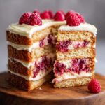 A slice cut from a White Chocolate Raspberry Cake, showcasing layers of cake, white chocolate frosting, and raspberry filling.