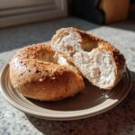 Freshly baked bagels recipe cottage cheese, one sliced open, on a plate with sesame seeds.