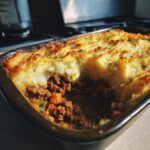 Close-up of a partially eaten best classic shepherds pie recipe in a baking dish, showing the meat filling and mashed potato topping.