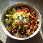 Overhead shot of a colorful chicken and rice bowl with avocado, salsa, cheese, and sour cream.