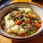 A bowl of crockpot shepherds pie soup recipe, featuring mashed potatoes, ground beef, carrots, peas, and corn.