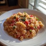 A serving of easy mexican rice recipe rotel on a white plate, garnished with herbs and diced tomatoes.