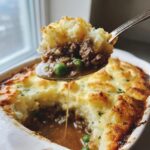 Spoonful of easy shepherds pie recipe gravy with meat, peas, and mashed potato topping.