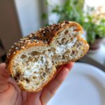 A halved everything bagel filled with cream cheese, held in a hand. Not related to blueberry protein breakfast cookies.