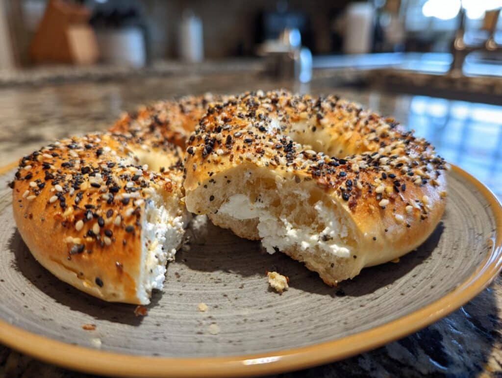 Everything bagel cut in half and filled with cream cheese on a gray plate.