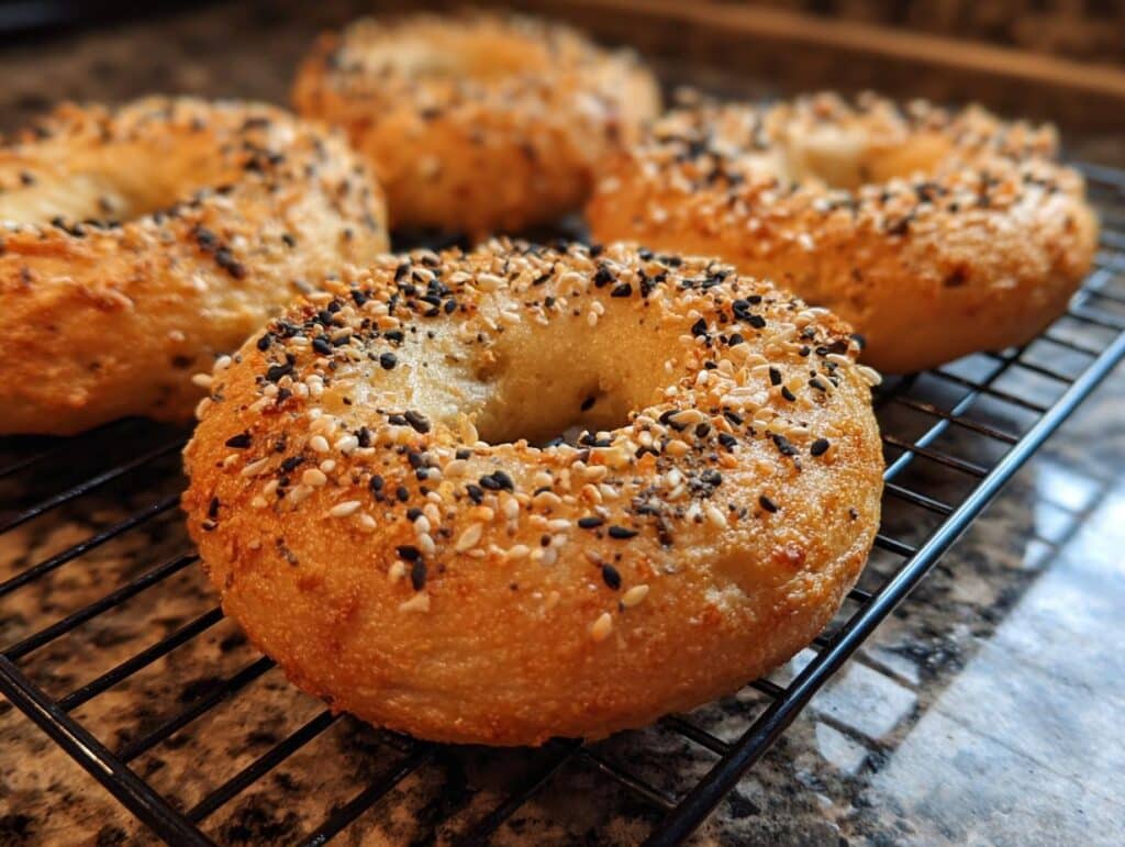 Four everything bagels with sesame, poppy, and other seeds on a black cooling rack. Not related to blueberry smoothie protein.