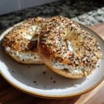 Two everything bagels with cream cheese filling on a plate, ready to eat.