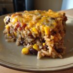 A slice of Mexican black beans and rice casserole with corn and melted cheese on a plate.