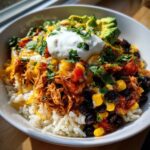 A vibrant Mexican chicken rice bowl with rice, chicken, black beans, corn, avocado, sour cream, and cheese.