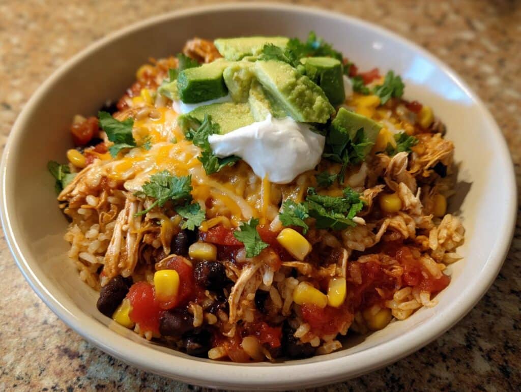 A delicious Mexican chicken rice bowl topped with avocado, sour cream, cheese, and cilantro.