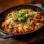 Skillet of cheesy mexican rice and beans with chicken, garnished with tomatoes, cilantro, and green onions.