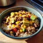 A vibrant Mexican rice bowl with sauce, featuring rice, seasoned ground beef, corn, avocado, and black beans.