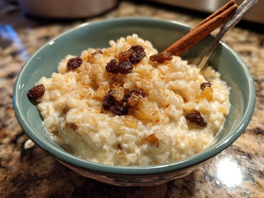 A bowl of creamy Mexican rice pudding recipe, topped with raisins and cinnamon, with a cinnamon stick.
