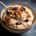 Spoonful of creamy Mexican rice pudding recipe crockpot, topped with cinnamon and raisins, ready to eat.