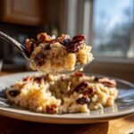 Spoonful of creamy Mexican rice pudding crockpot topped with pecans and raisins, dripping with deliciousness.