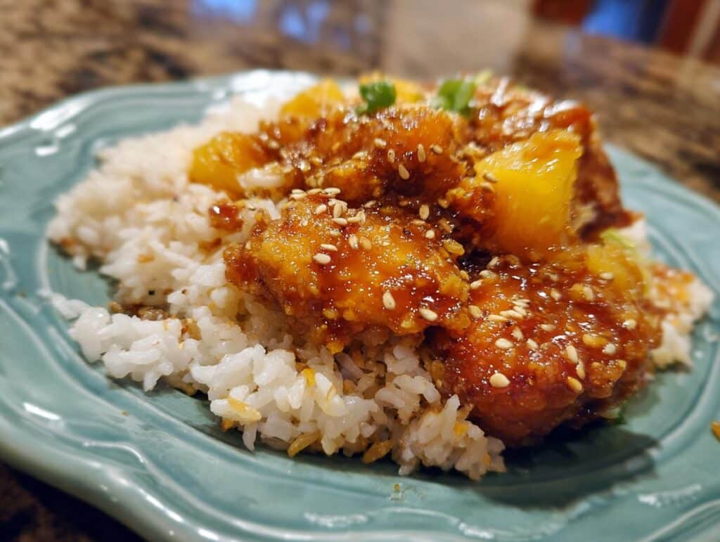 Close-up of pineapple chicken rice easy recipe, served on a blue plate with sesame seeds and green onions.
