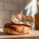 Two protein bagels with greek yogurt cinnamon sugar, one sliced in half, stacked on a wooden board.