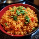 Bowl of authentic restaurant mexican rice recipe, garnished with cilantro and diced tomatoes.