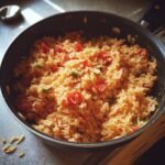 A pan filled with cooked rice, diced tomatoes, and green peppers.